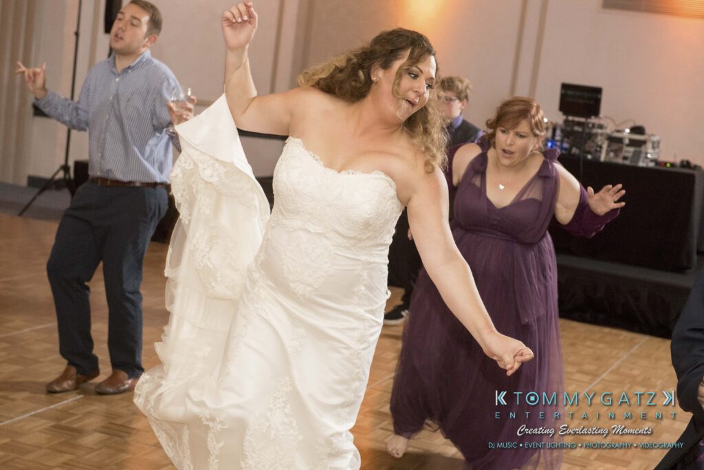 A bride energetically dancing at a wedding reception, accompanied by guests on the dance floor.