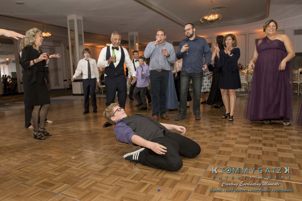 Person in purple shirt dancing on the floor while people watch and laugh at a formal event.