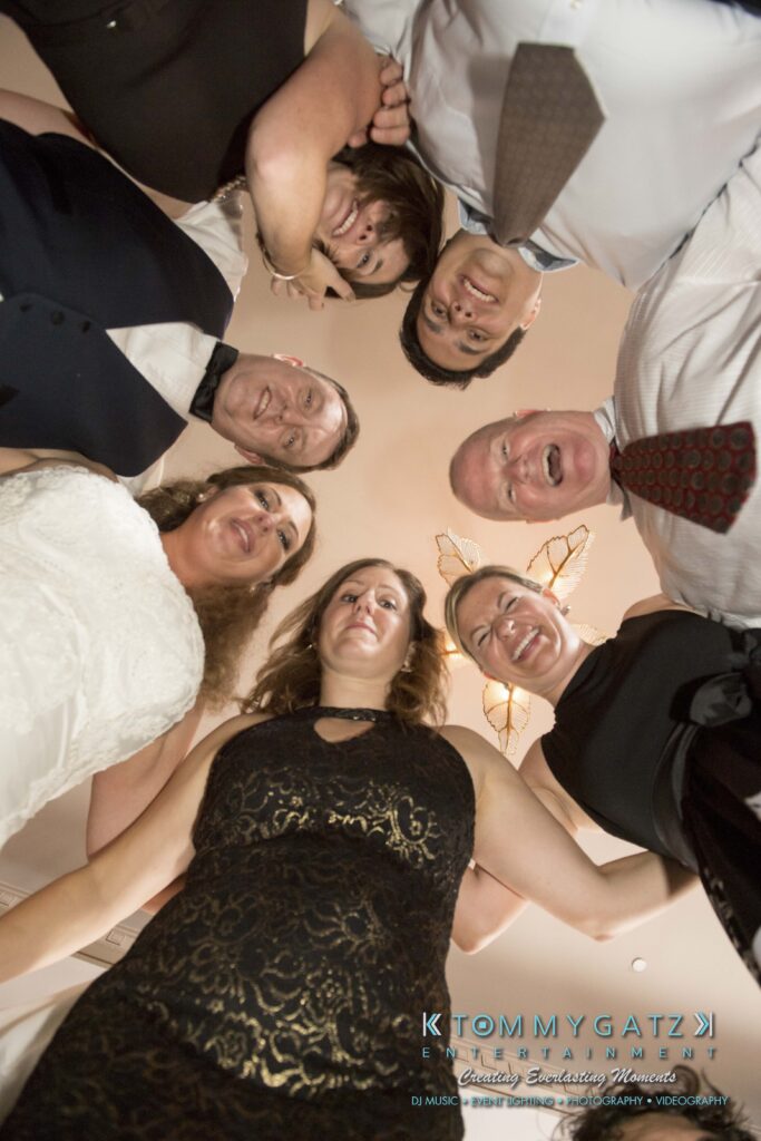 A group of people dressed formally in a circle, looking down at the camera, indoors.