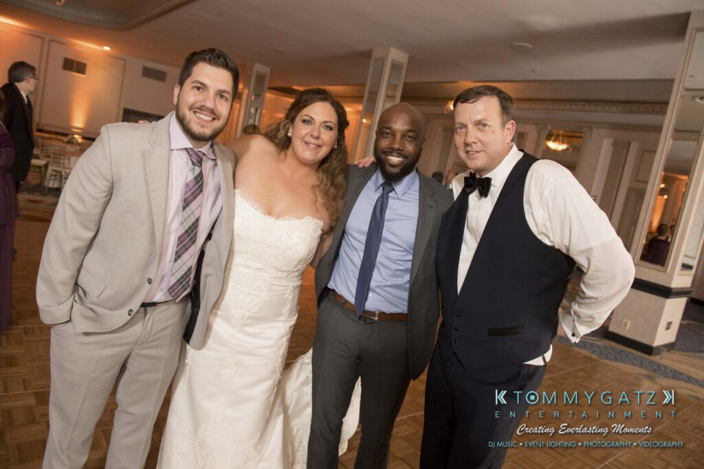 Four people pose together at an event; one is wearing a wedding dress, and the others are in formal attire.