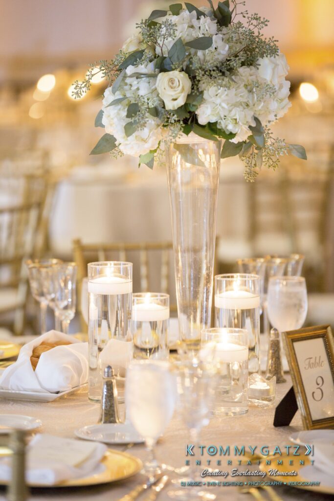 Elegant table setting with a tall floral centerpiece, candles in glass holders, and a table number card.