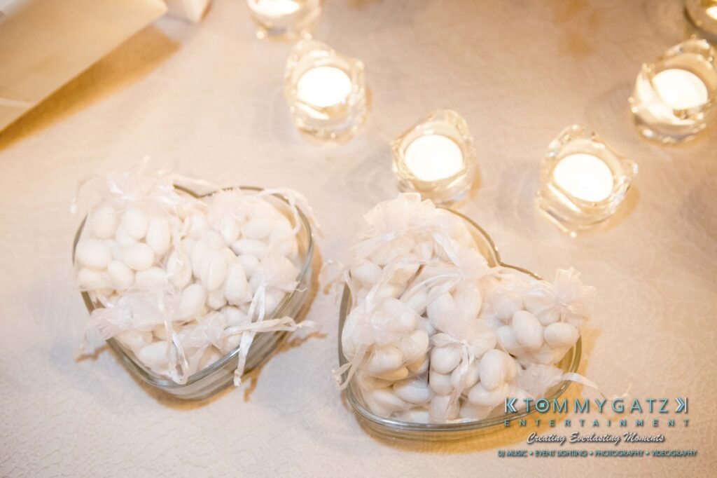 Two heart-shaped glass bowls filled with white candies, placed on a table adorned with lace. Lit candles in holders are visible in the background.