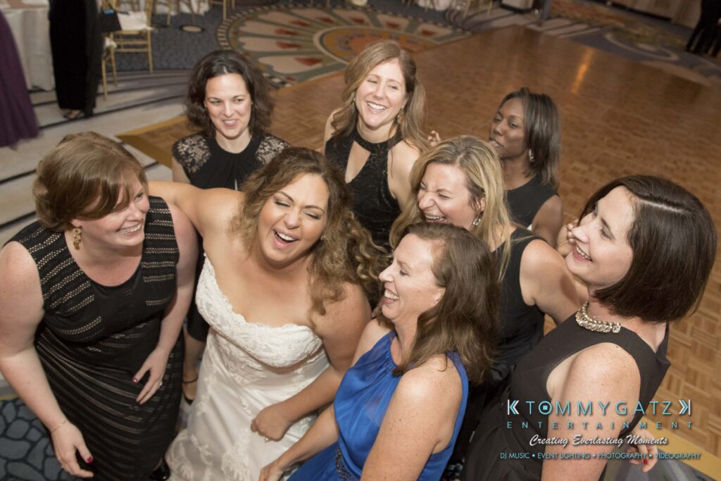 Bride laughing with a group of eight women on a dance floor.