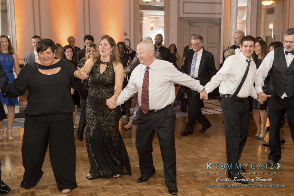 People in formal attire holding hands and dancing in a ballroom.