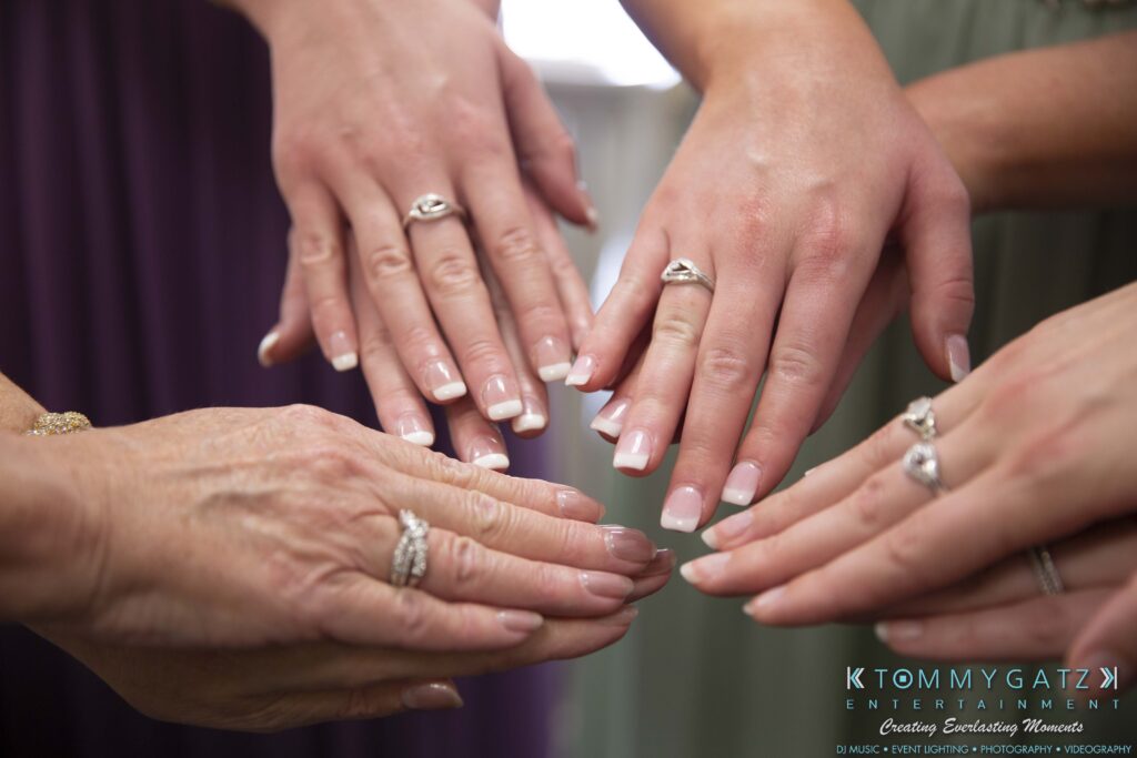 Six hands with manicured nails showing rings.