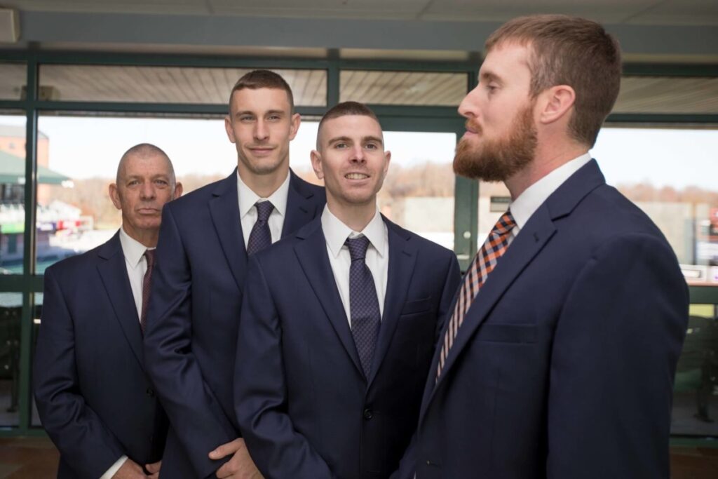 Four men in suits standing in line indoors, with a windowed background.