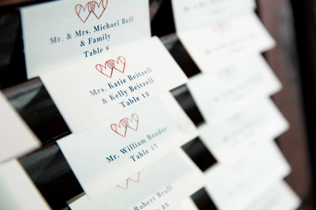 Close-up of wedding place cards featuring names and table assignments, with heart motifs at the top of each card.