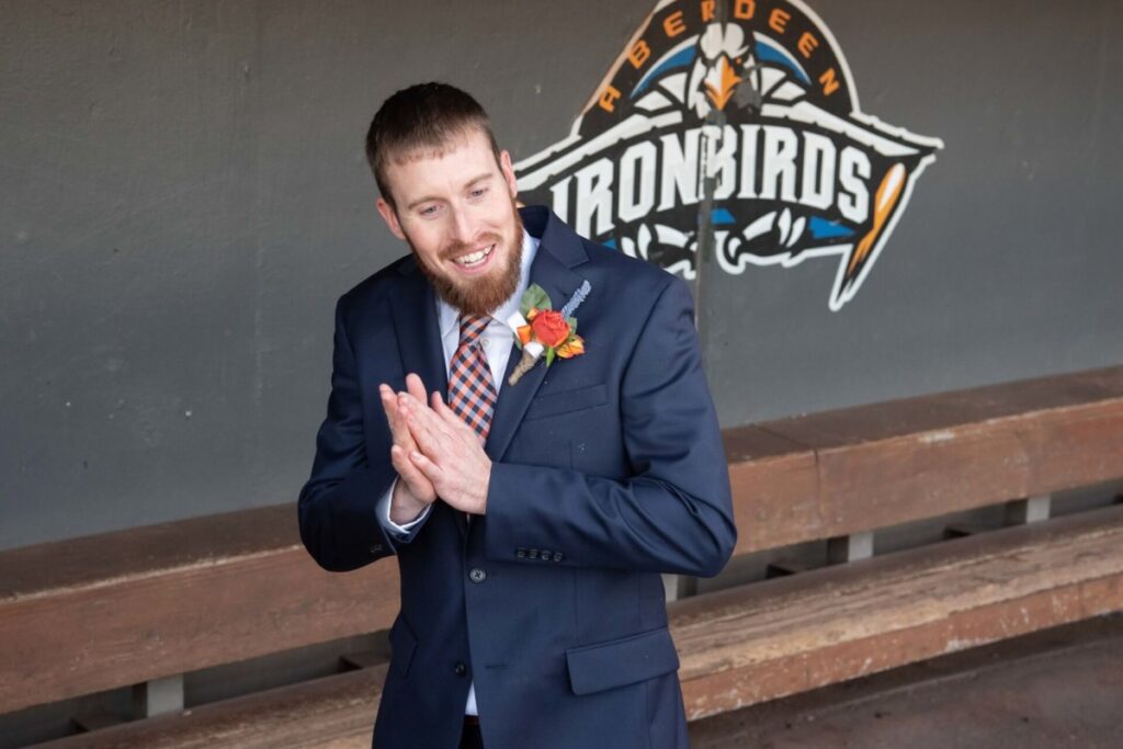 Man in a suit with a boutonniere stands smiling in front of an "Aberdeen IronBirds" logo in a dugout.