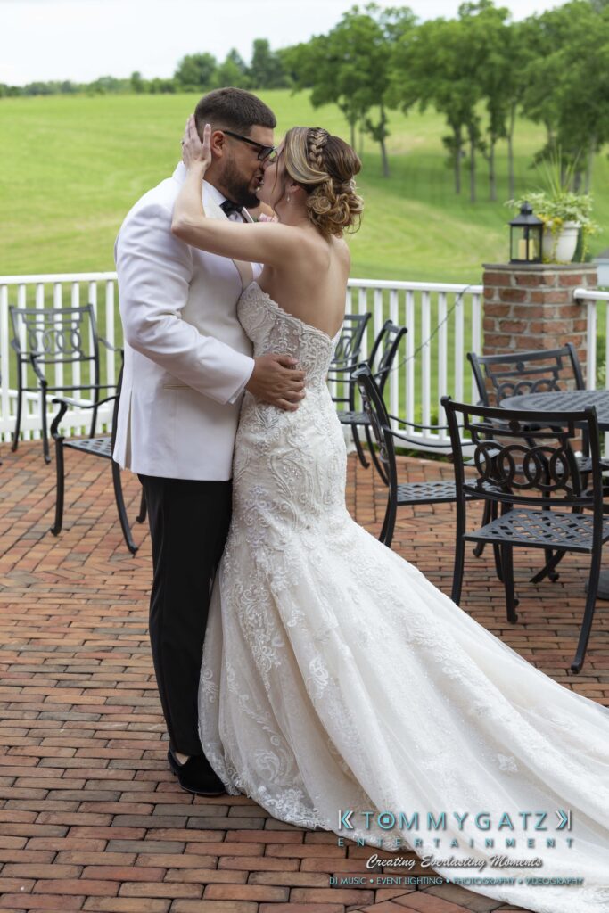 A bride and groom share a kiss on a brick patio with a grassy field in the background.