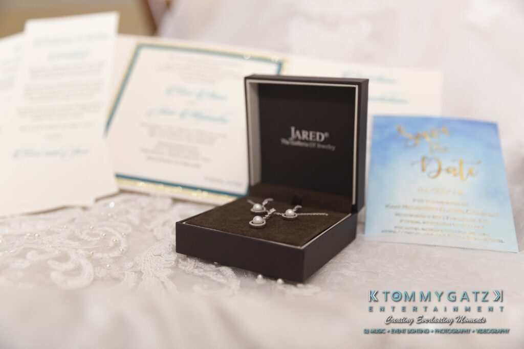 A jewelry box with a necklace and earrings is open on a cloth surface. Wedding invitations and a save-the-date card are in the background.
