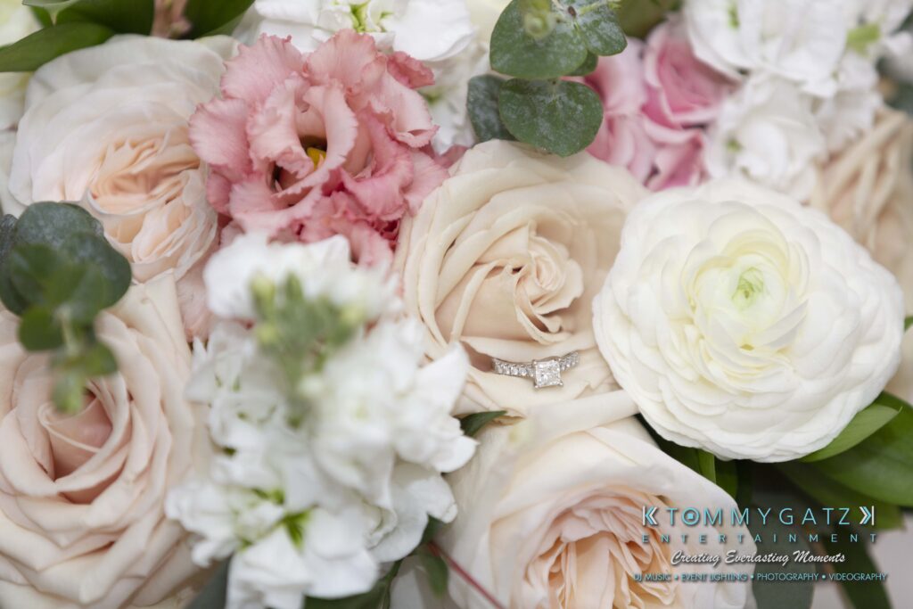A close-up of a bouquet featuring pale pink and white roses, with a diamond ring placed among the petals.