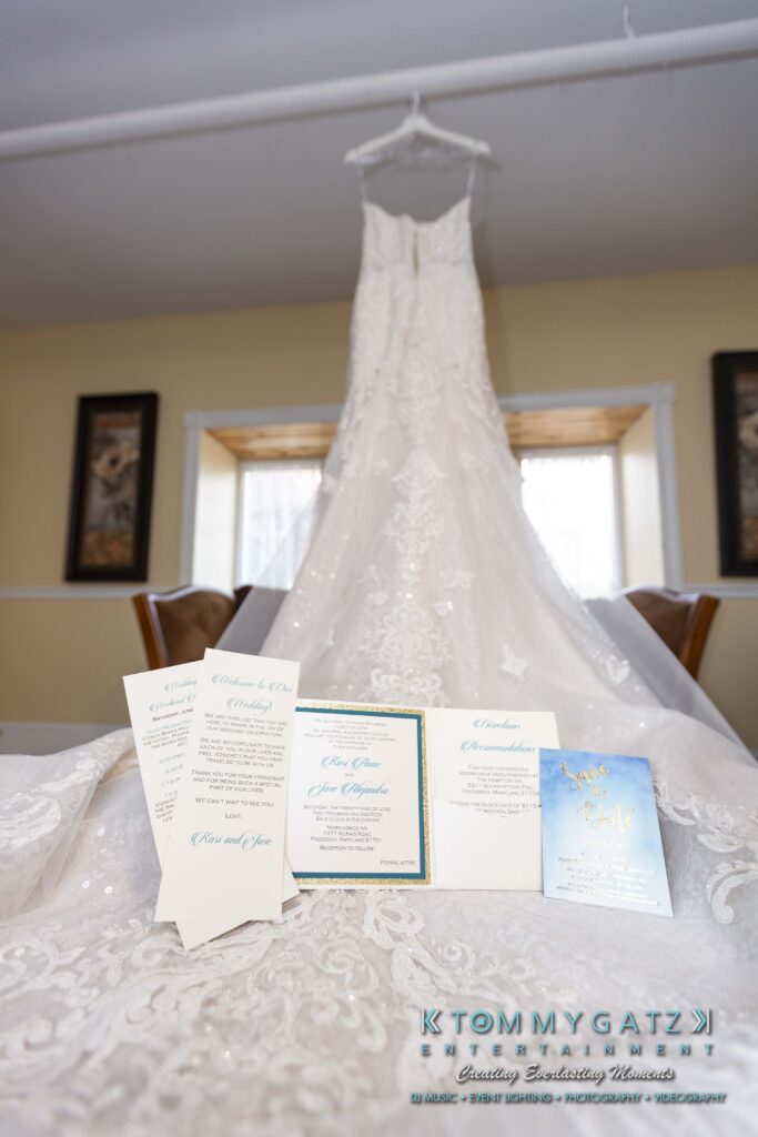 A white wedding dress hangs above a display of wedding invitations and cards, set on a wooden table in a softly lit room.