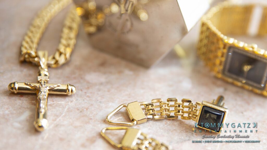 Gold jewelry including a cross pendant necklace, two watches, and a chain bracelet displayed on a marble surface.