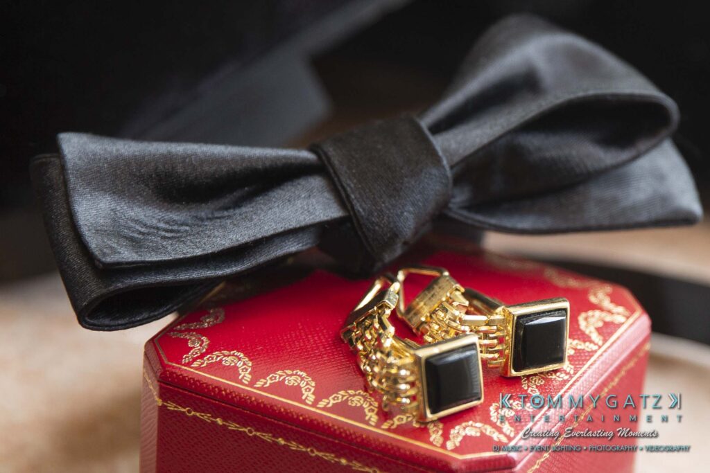 Black bow tie and gold cufflinks on a red box with ornate details.