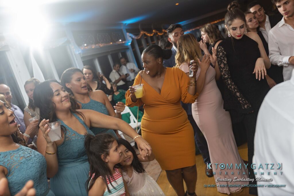 People dancing and smiling at a lively indoor party, some holding drinks.