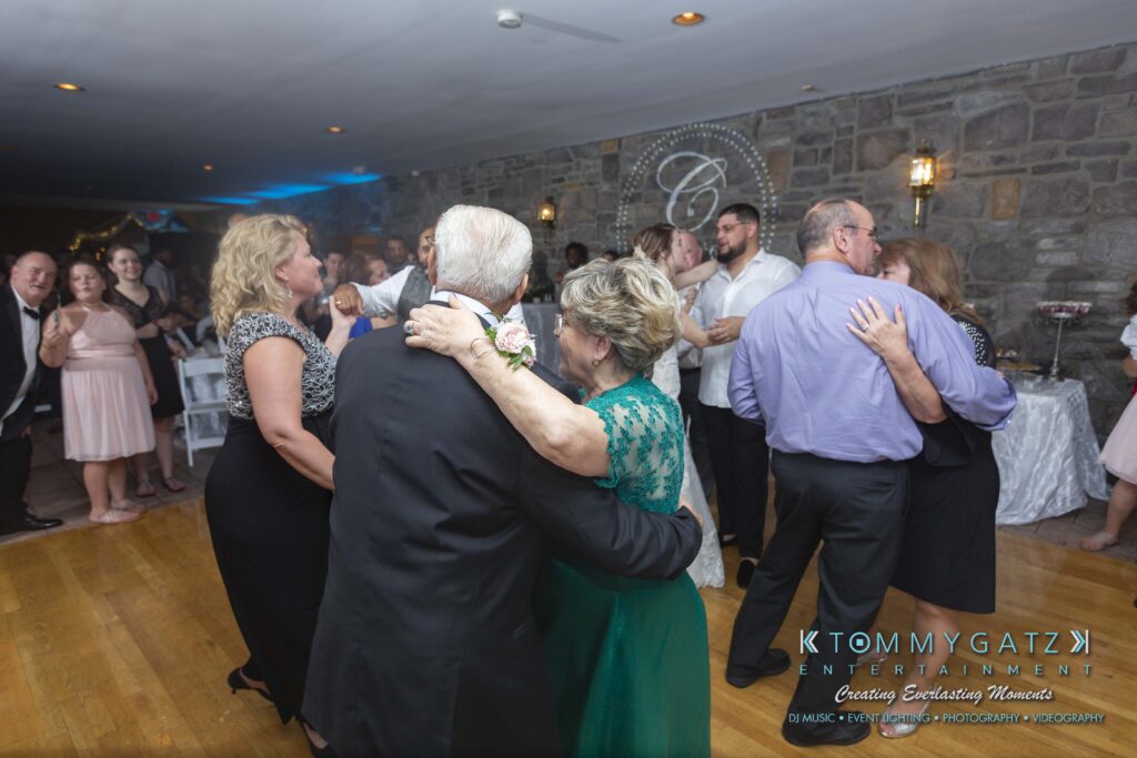 Couples dance in a banquet hall with stone walls; people in formal attire enjoy the event.