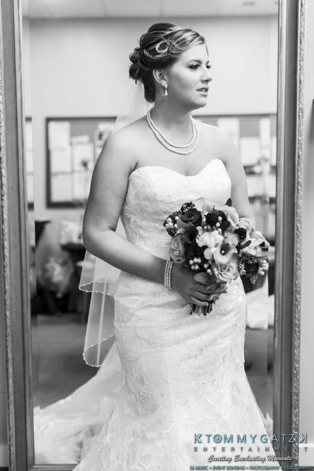 Bride in strapless lace gown holding a bouquet, standing in front of a mirror.