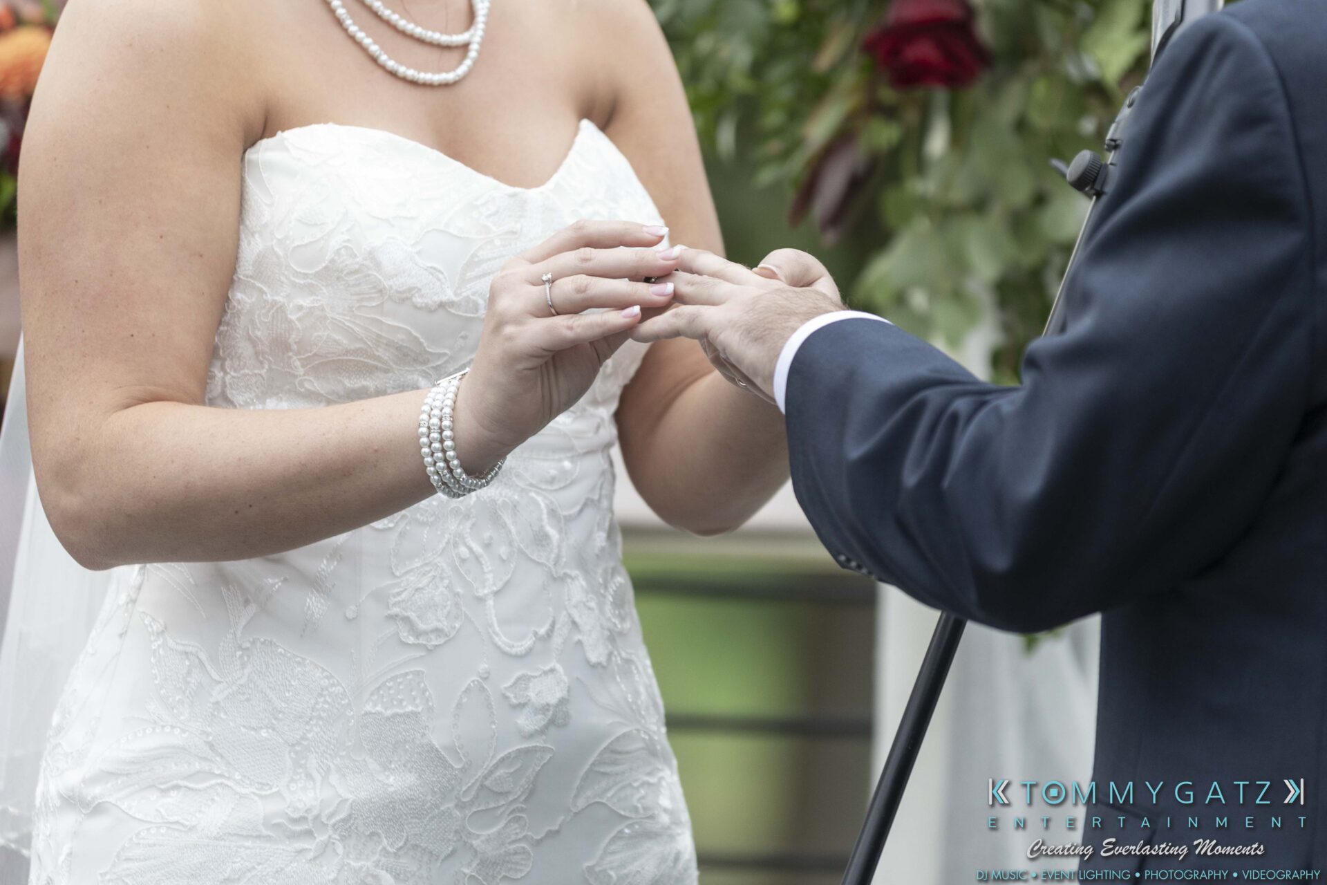 Bride and groom exchanging rings during wedding ceremony, with bride in white lace dress and pearl jewelry.