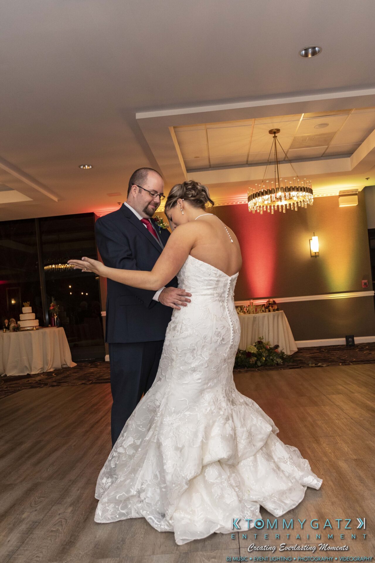 A couple dances in a decorated room, with the woman wearing a white dress and the man in a suit.