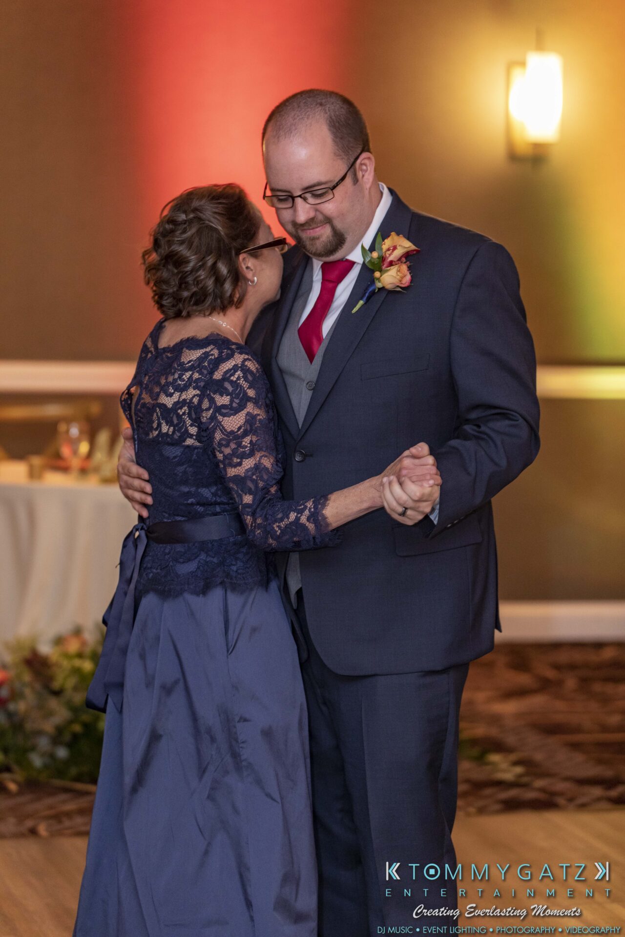 A man and woman, dressed formally, share a close dance in a warmly lit room.