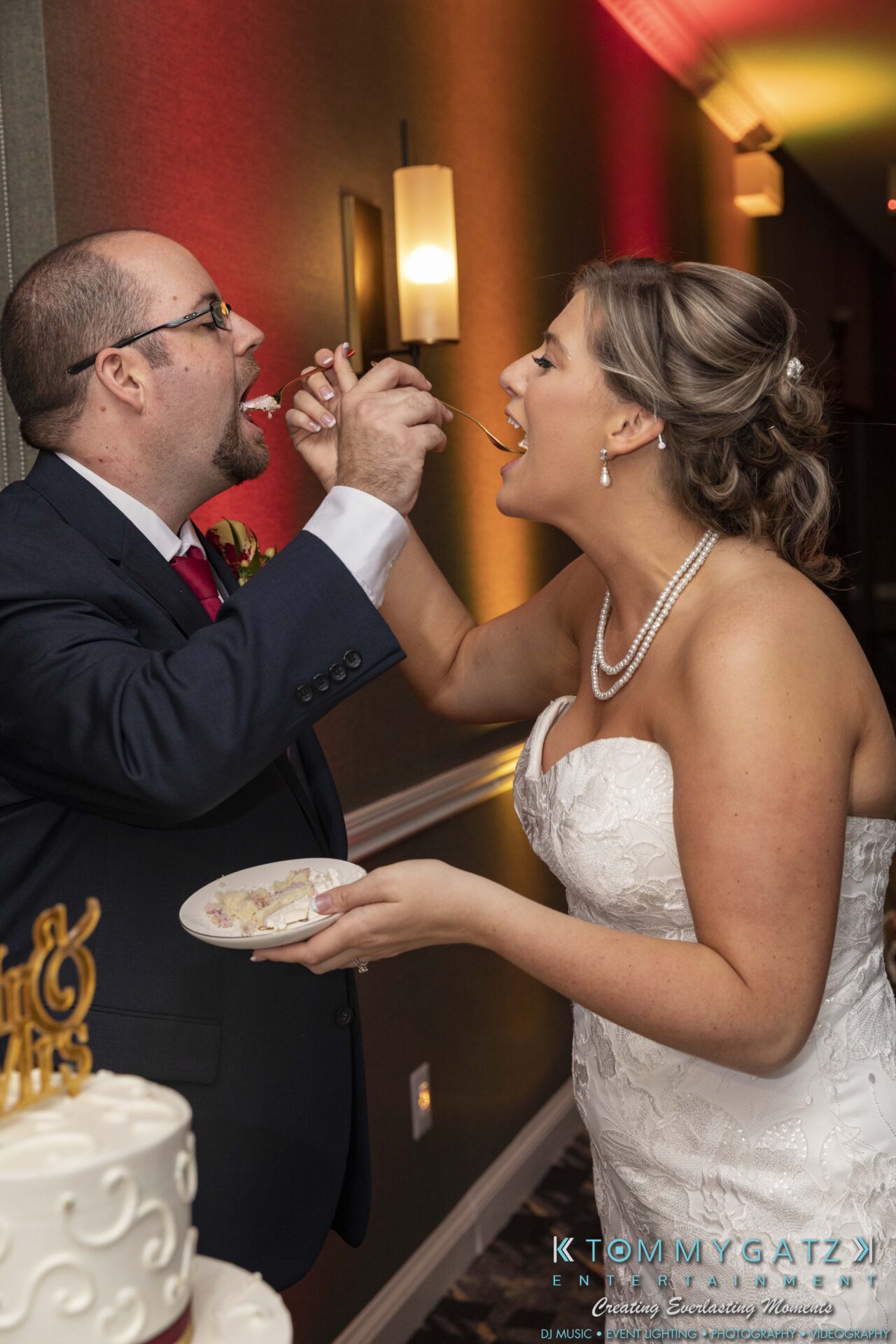 A bride and groom feed each other cake at a wedding, standing next to a decorated table.