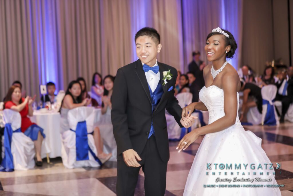 A couple in formal wear is dancing in a decorated venue with seated guests in the background.