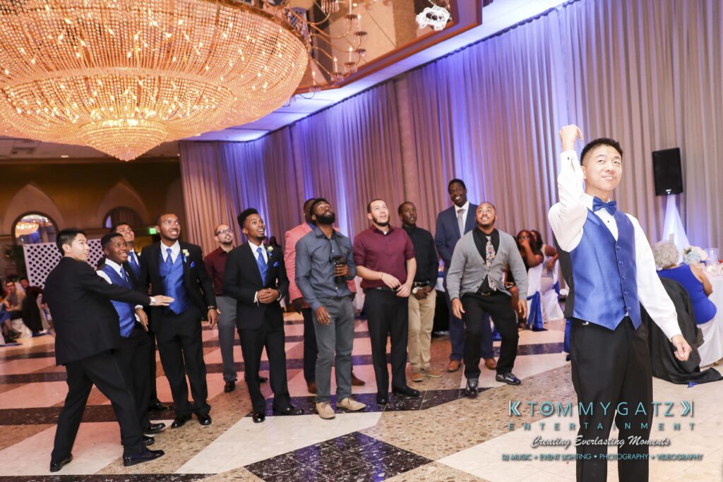 A groom is preparing to toss a garter while a group of men eagerly watch and prepare to catch it at a wedding reception.