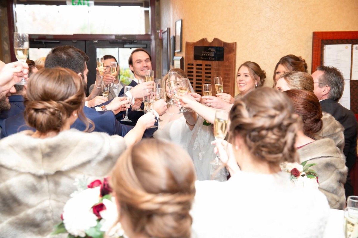 A group of people raising glasses in a celebratory toast, indoors with a plaque visible on the wall.