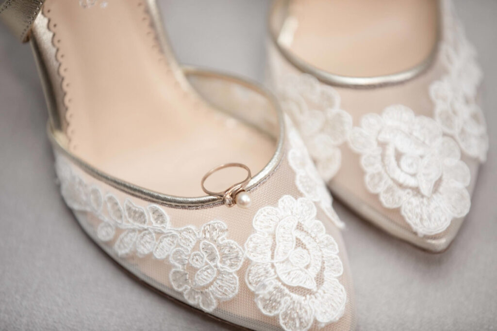 A pair of lace-decorated shoes with a ring placed on one of them.