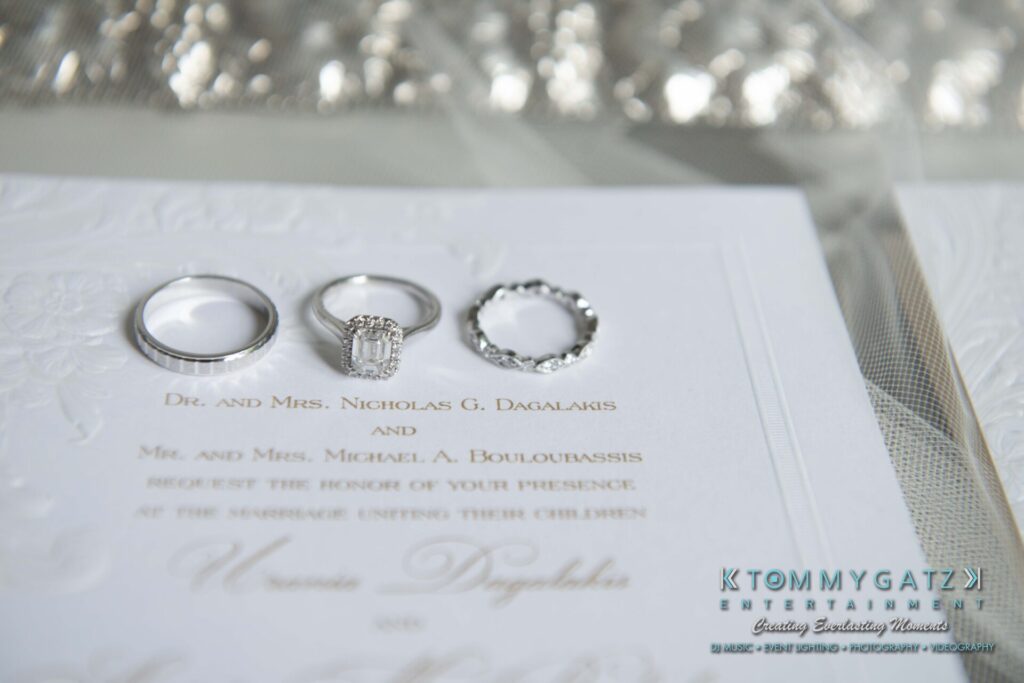 Three wedding rings placed on a formal invitation card. The card includes printed text and embossed details.
