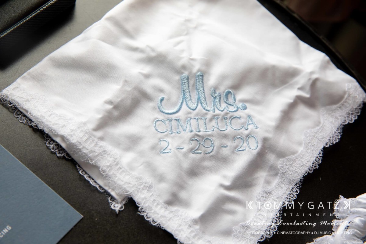 White handkerchief with lace edges, embroidered with "Mrs. Cimilluca 2-29-20" in blue thread.