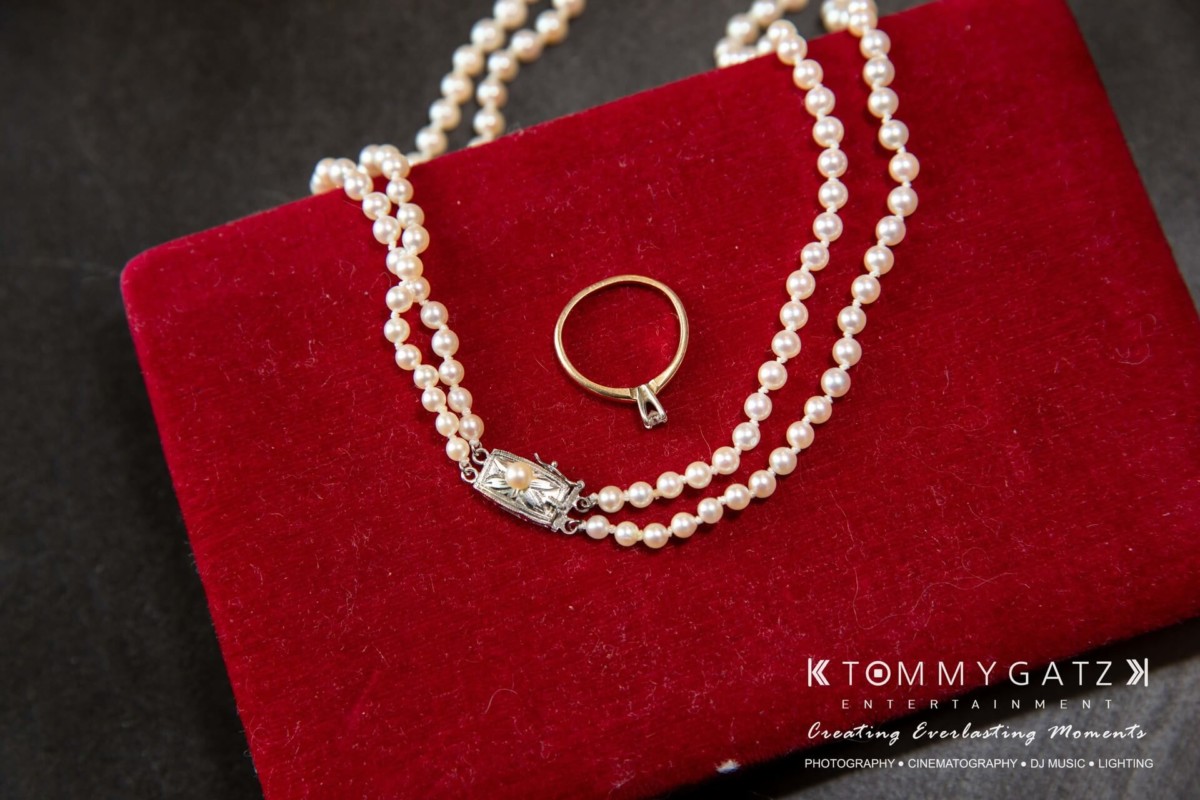 A pearl necklace and a gold ring on a red velvet surface.