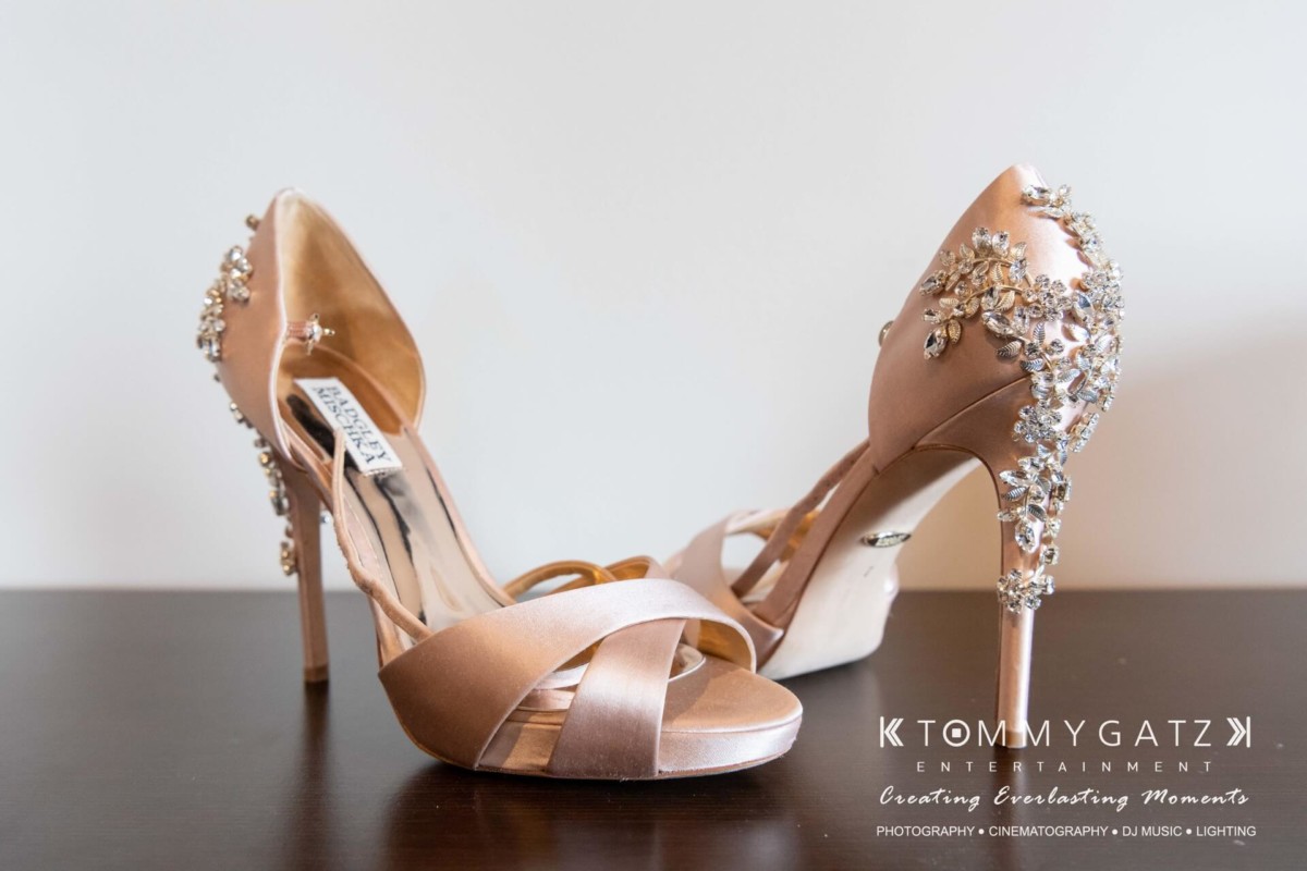 Elegant high-heeled shoes adorned with rhinestones on a wooden surface. Tommy Gatz Entertainment logo in the corner.