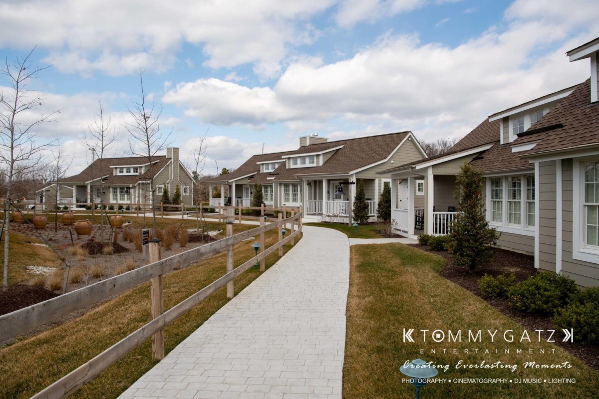 Sidewalk between landscaped gardens and suburban houses under a partly cloudy sky.