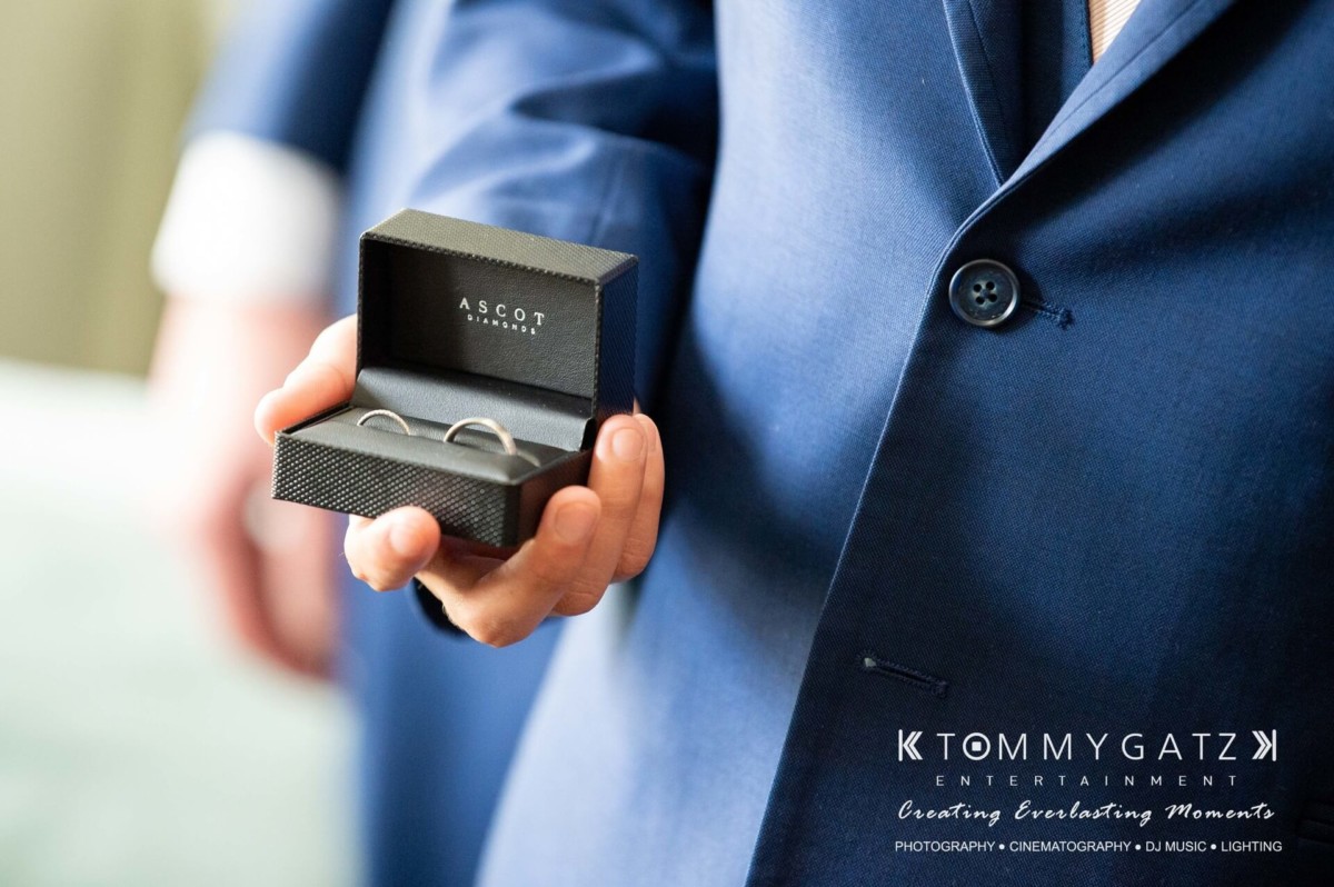 A person in a blue suit holds a small black box containing two rings.