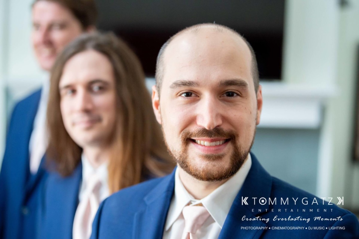Three men in suits smiling, with one in focus while the others are blurred in the background.