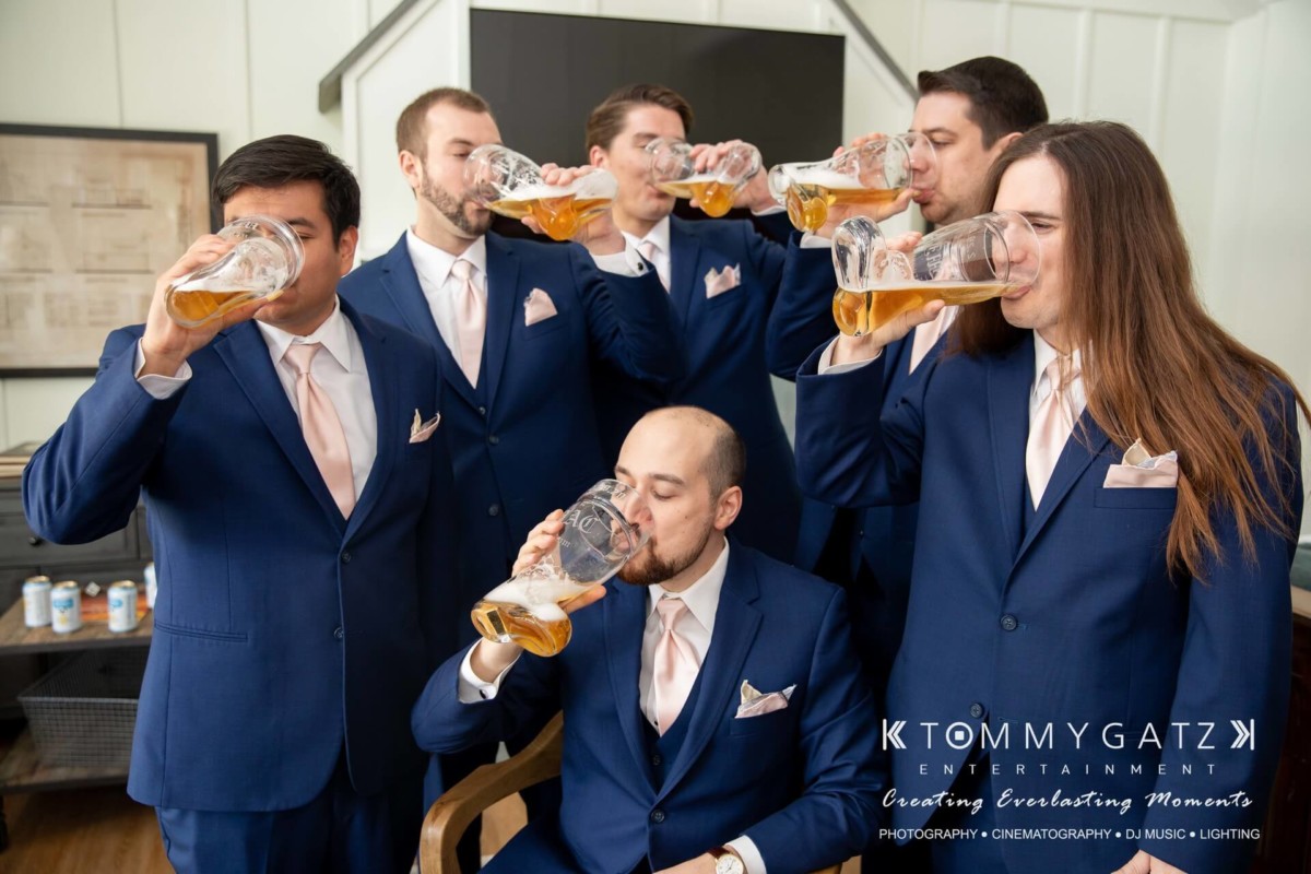 A group of six men in blue suits drink beer from large mugs indoors.