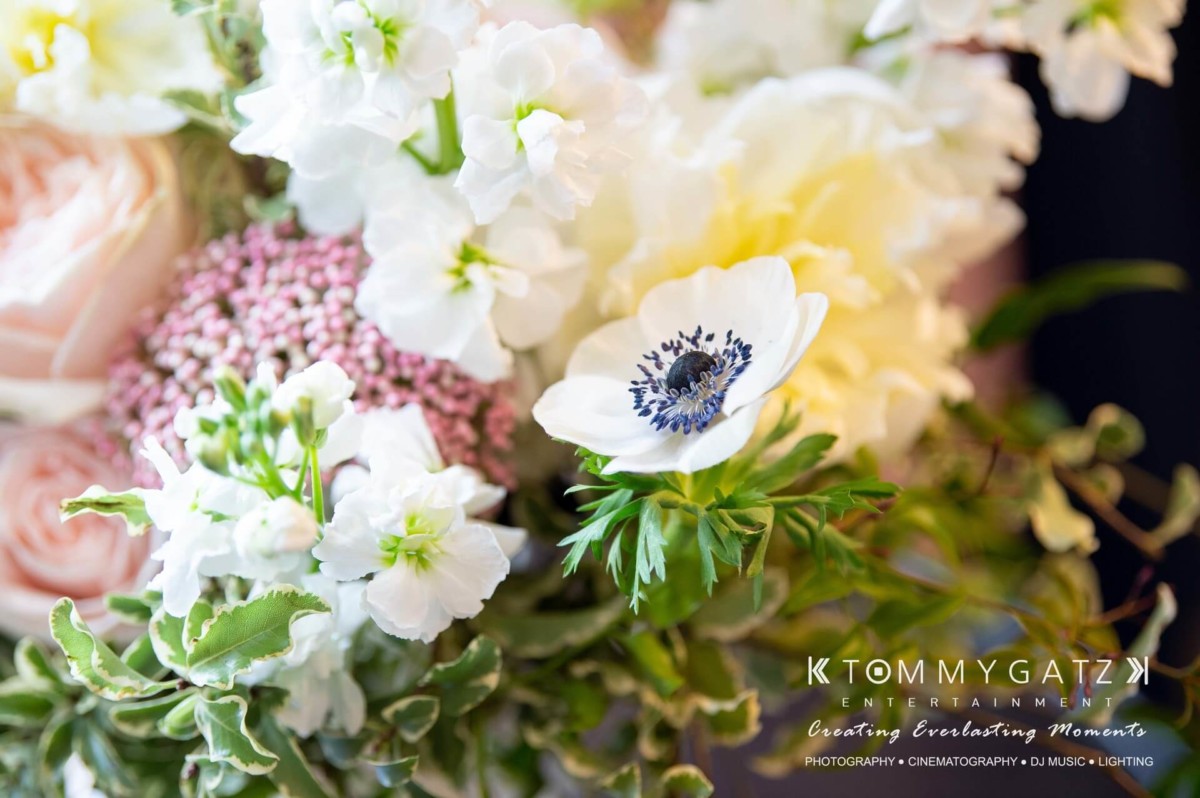 A close-up of a detailed floral arrangement featuring pink roses, white anemones, and various greenery.