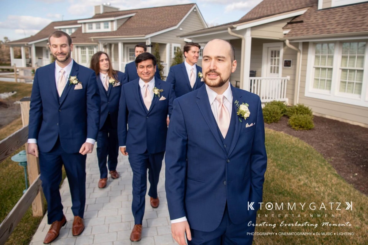 A group of six men in blue suits walk on a path outside a house.