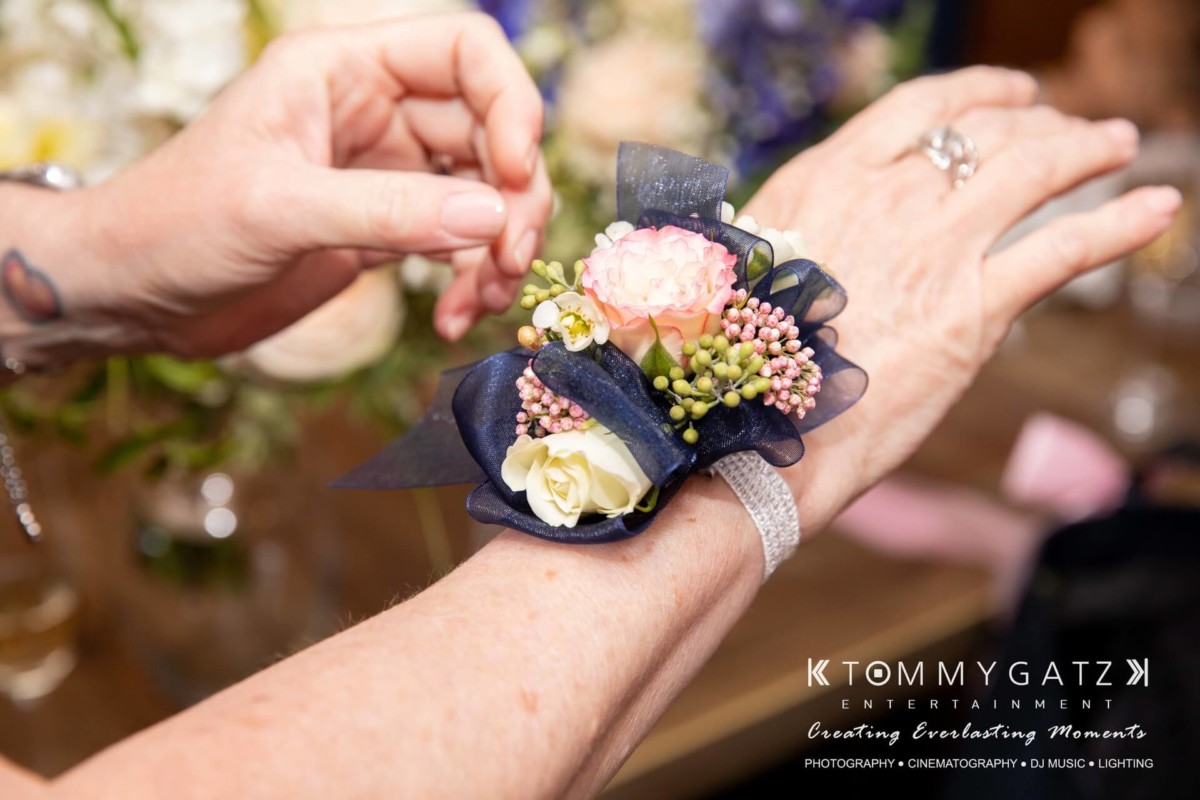 A person wears a floral corsage with pink, white, and green flowers on their wrist.