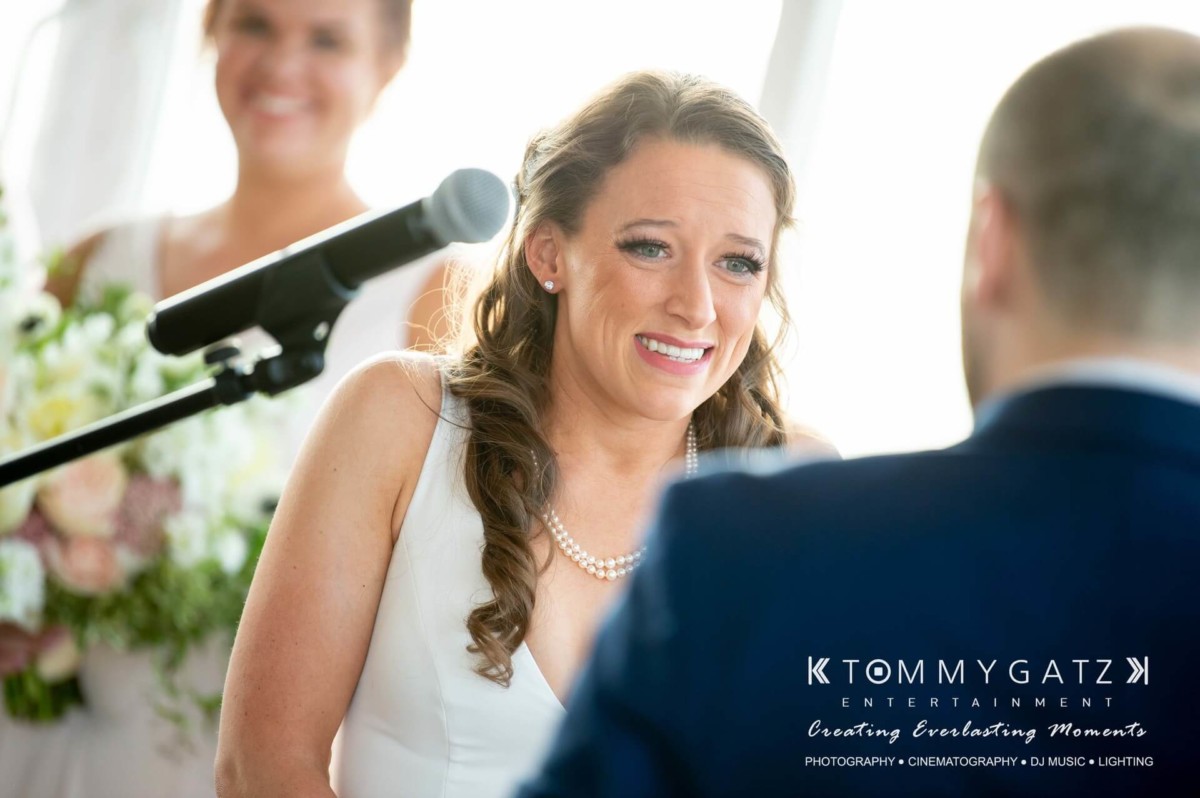 A woman in a white dress stands near a microphone, appearing emotional. A bouquet is in the background. The image has text at the bottom about Tommy Gatz Entertainment.