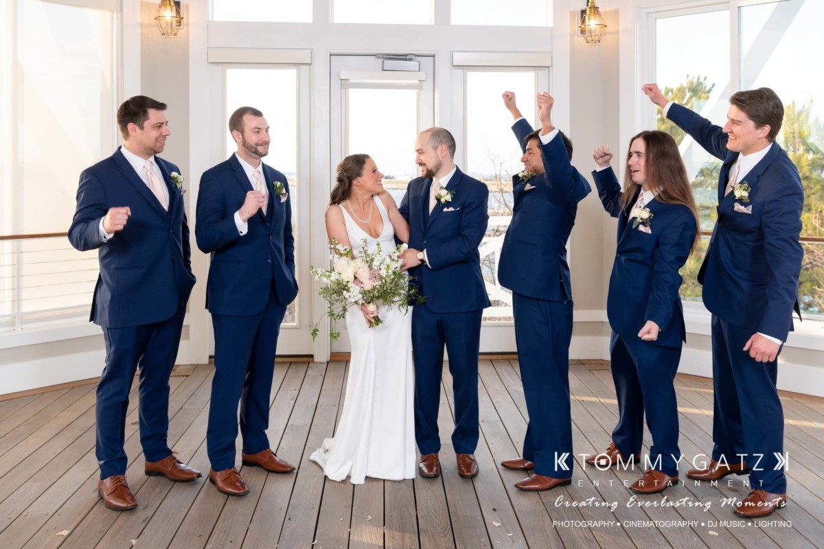 Bride and groom stand together with groomsmen in blue suits celebrating on a covered porch.