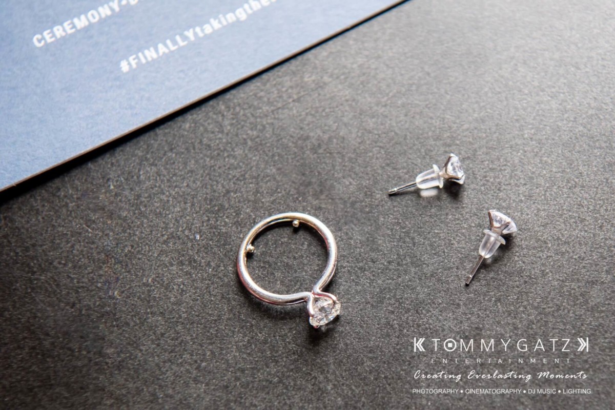A diamond ring and a pair of stud earrings are placed on a dark surface near a card with text.