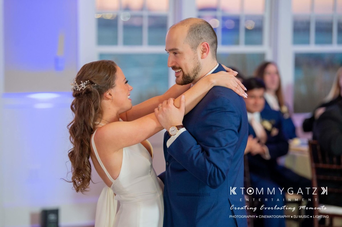 A bride and groom share their first dance at a wedding reception, with guests seated in the background.