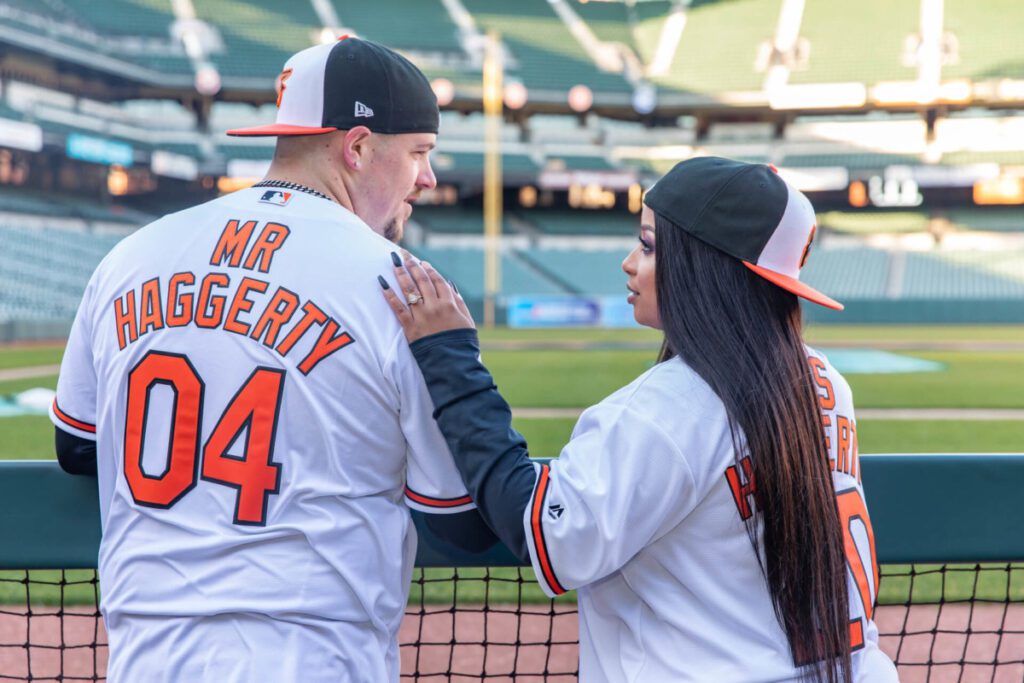 A couple in matching baseball jerseys, with "Mr. Haggerty" and "Mrs. Haggerty" on the back, stands in a stadium facing the field.