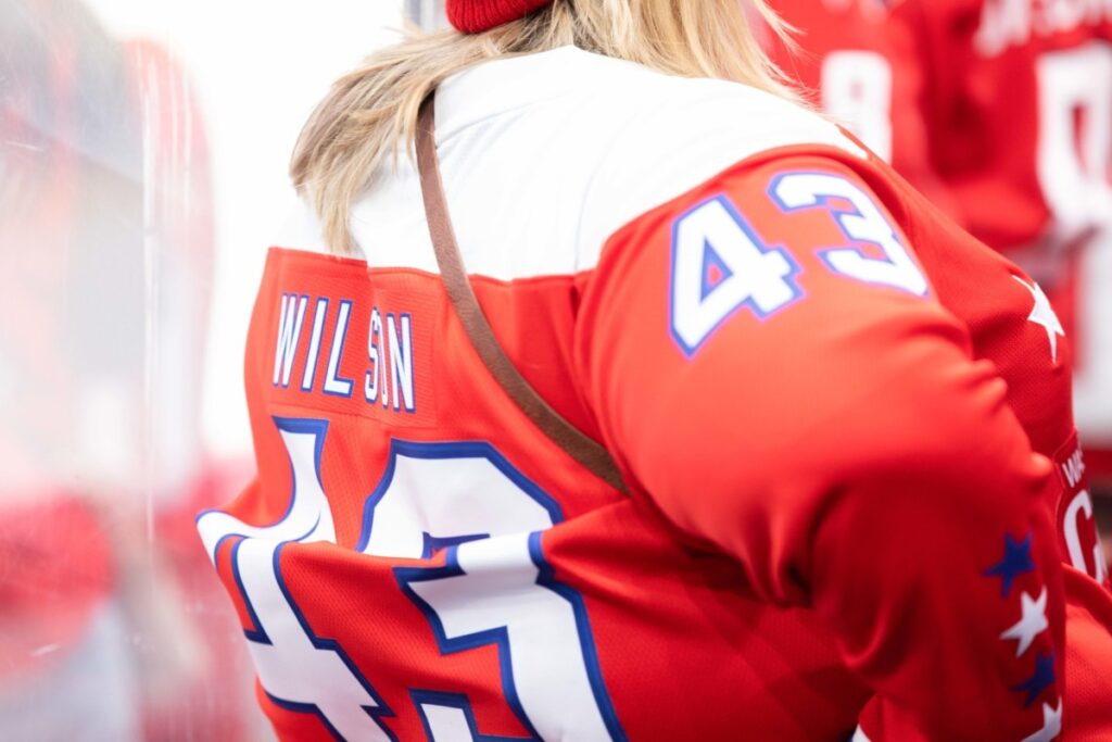 Person wearing a red hockey jersey with "Wilson" and number 43 on the back, standing near a glass barrier.