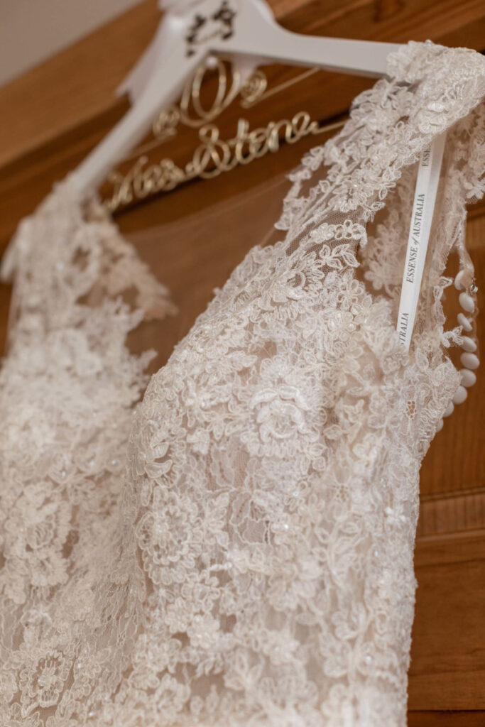 Close-up of a lace wedding dress on a hanger, displaying intricate floral patterns and buttons on the back.
