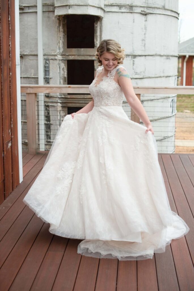 Woman in lace wedding dress smiling and twirling on a wooden deck with large silo in the background.