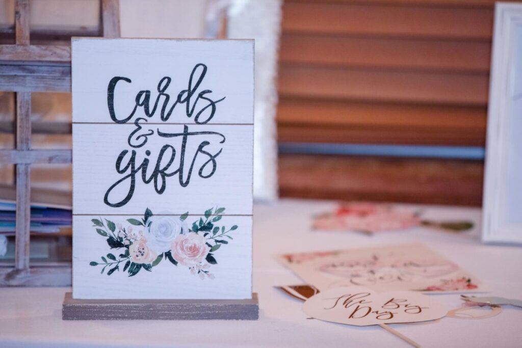 A wooden sign on a table reads "Cards & gifts" with floral decoration. Nearby are cards and a circular tag with "The Big Day" text.