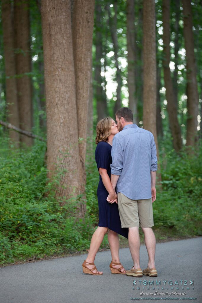 A couple holding hands, walking on a forest path, both in casual summer clothes. The forest is lush and green.